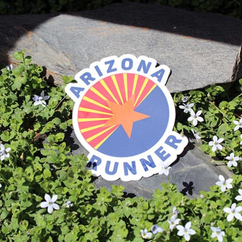 Arizona Running Sticker laying on rocks with white flowers for website