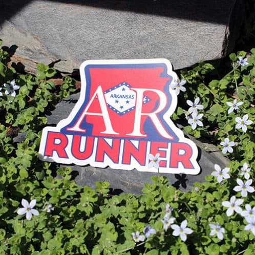 Arkansas Running Sticker laying on rocks with white flowers for website