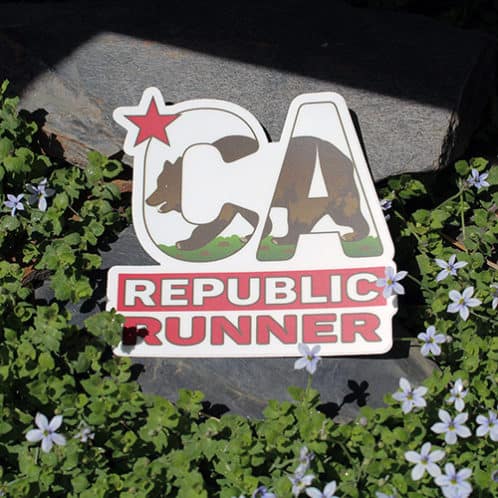 California Running Sticker laying on rocks with white flowers for website