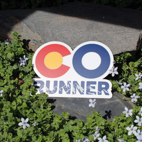 Colorado Running Sticker laying on rocks with white flowers for website