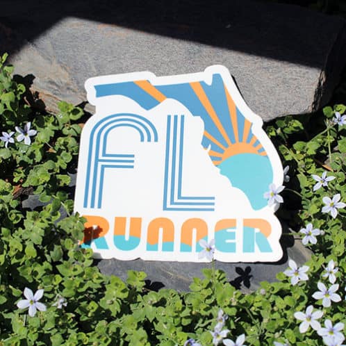 Florida Running Sticker laying on rocks with white flowers for website