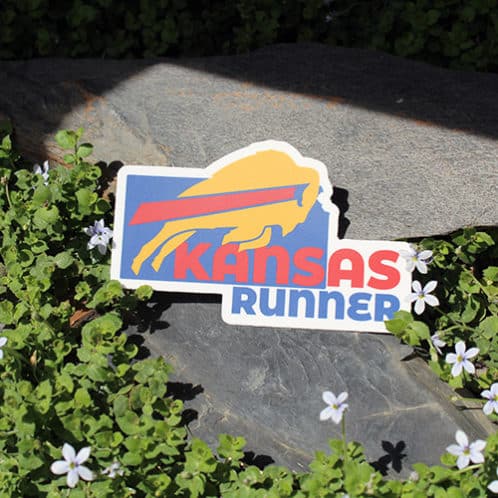 Kansas Running Sticker laying on rocks with white flowers for website