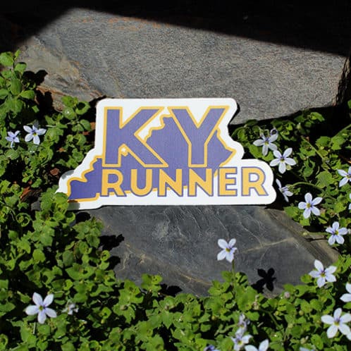 Kentucky Running Sticker laying on rocks with white flowers for website
