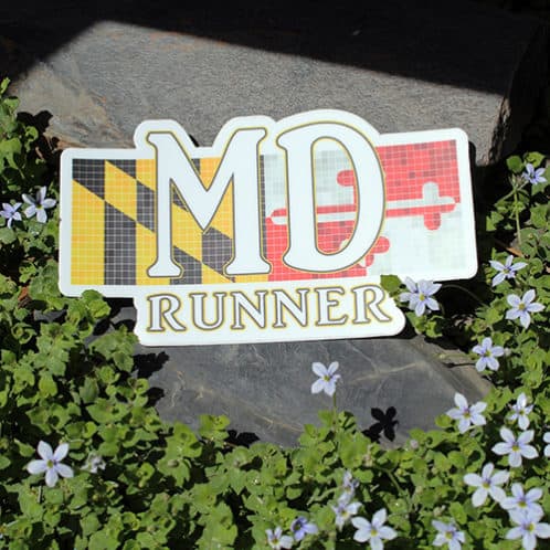 Maryland Running Sticker laying on rocks with white flowers for website