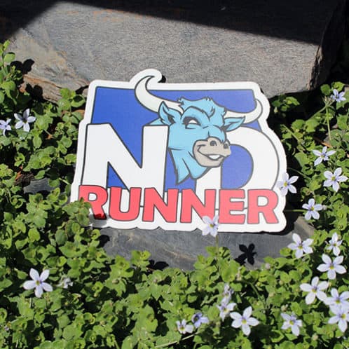 North Dakota Running Sticker laying on rocks with white flowers for website