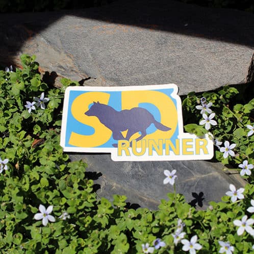 South Dakota Running Sticker laying on rocks with white flowers for website