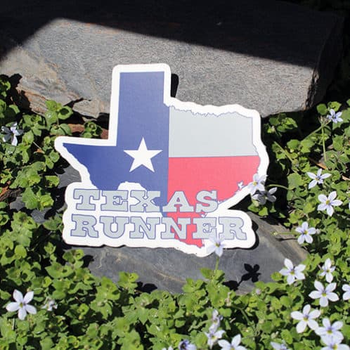 Texas Running Sticker laying on rocks with white flowers for website