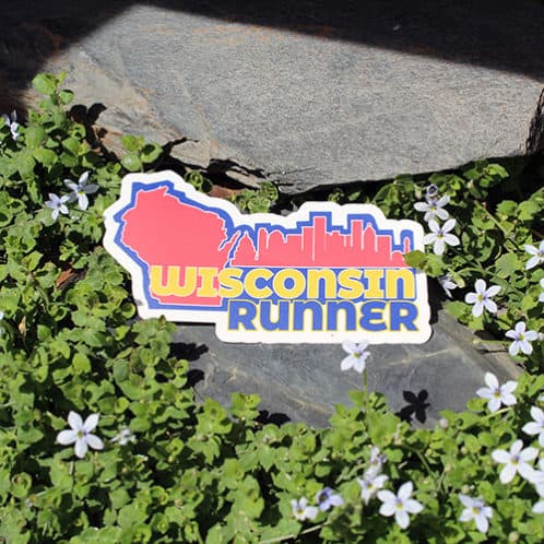 Wisconsin Running Sticker laying on rocks with white flowers for website