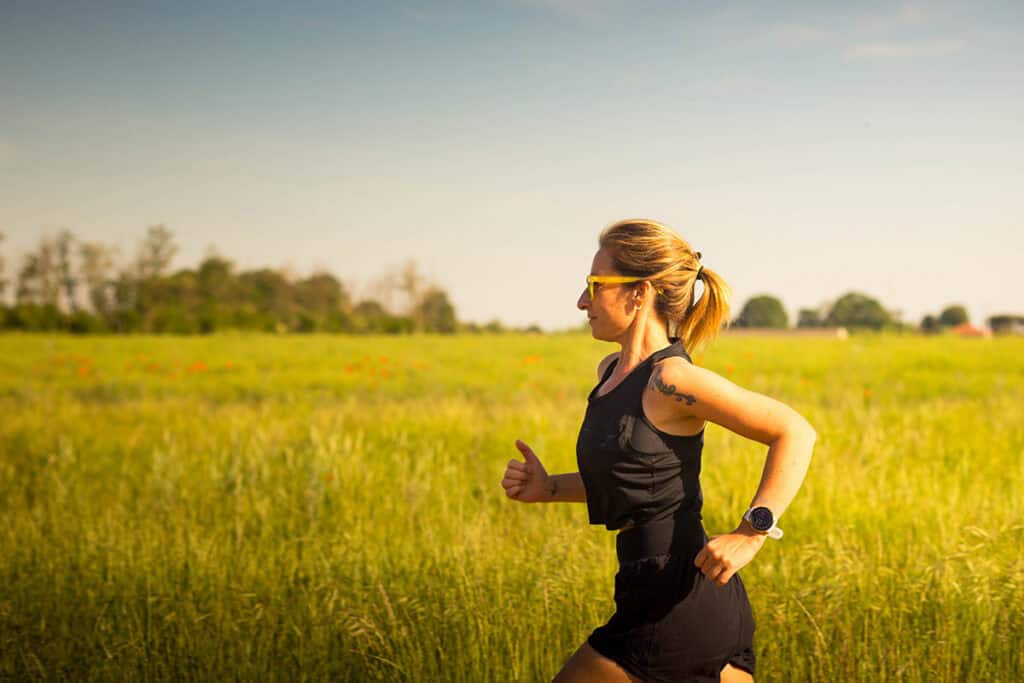 Runner training outdoors in a grassy field during golden hour, representing weekly running mileage, consistency, endurance training, and healthy recovery for runners.