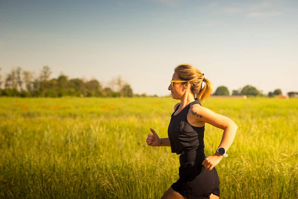 Runner training outdoors in a grassy field during golden hour, representing weekly running mileage, consistency, endurance training, and healthy recovery for runners.