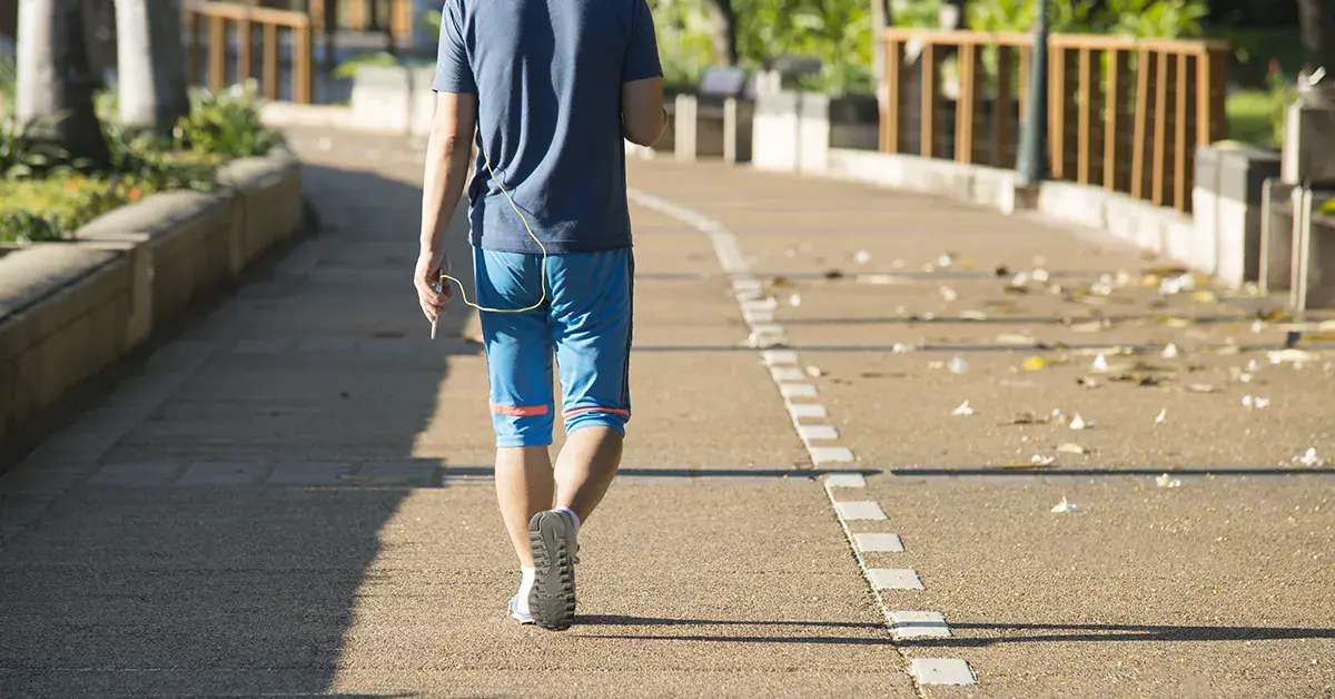Man walking on a sunny park path in running shorts and shoes